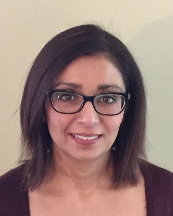 A smiling woman with shoulder-length dark hair and glasses, wearing a maroon top, standing against a light-colored wall, representing the Creve Coeur Behavioral Counseling team.