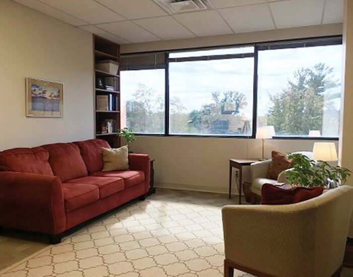 Comfortable counseling office with red sofa, armchair, large window view, and calming decor for Creve Coeur Behavioral Counseling and mental health support.